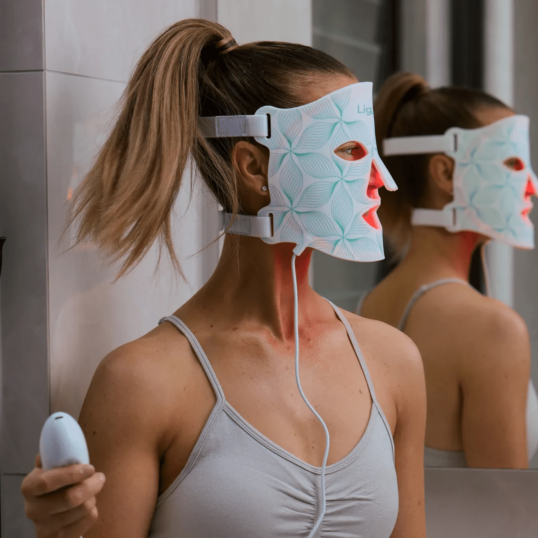 Kvinne bruker LUNOVA Pro LED maske med rødt lys foran speil, en del av LUNOVA Pro + C-Serum Pakke for effektiv hjemmespa hudpleie.